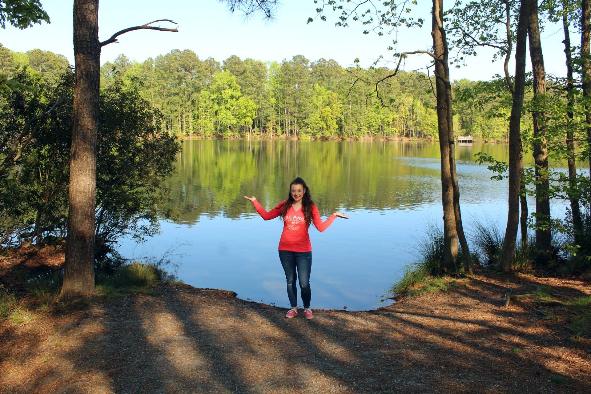 girl standing at the edge of lake with trees reflected in the water