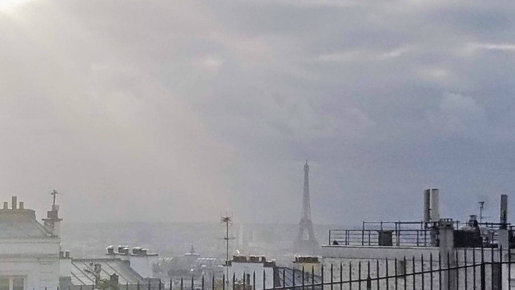 The eiffel tower lit up in a sunbeam as seen from Montmartre