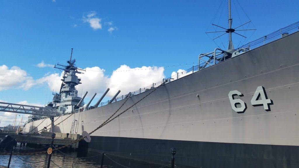 battleship wisconsin under a blue sky with fluffy clouds. docked in the norfolk harbor