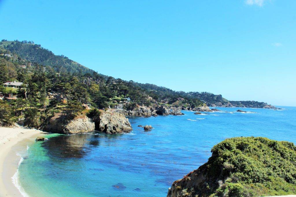 Looking down on a quiet beach with rocky cliffs and blue water and tree-covered hillsides