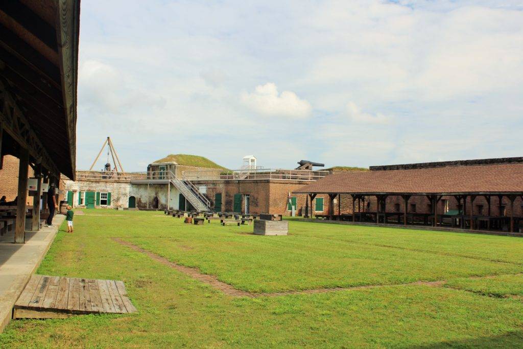 Green courtyard with brick fortifications on either side and cannons on top of the ramparts. Old Fort Jackson