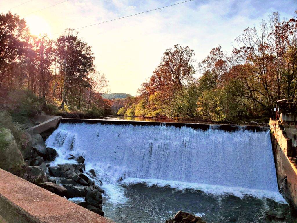 Water rushing over the Schuyler Dam with a background of trees and mountains