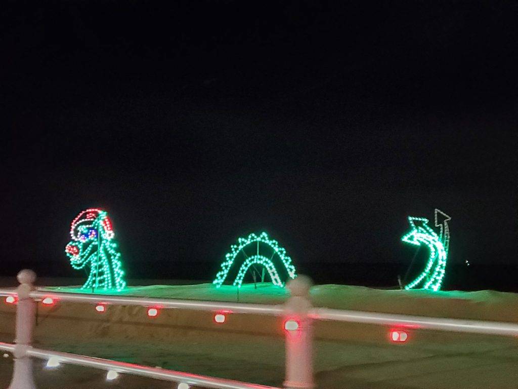Loch ness monster wearing a santa hat holiday lights on the beach event