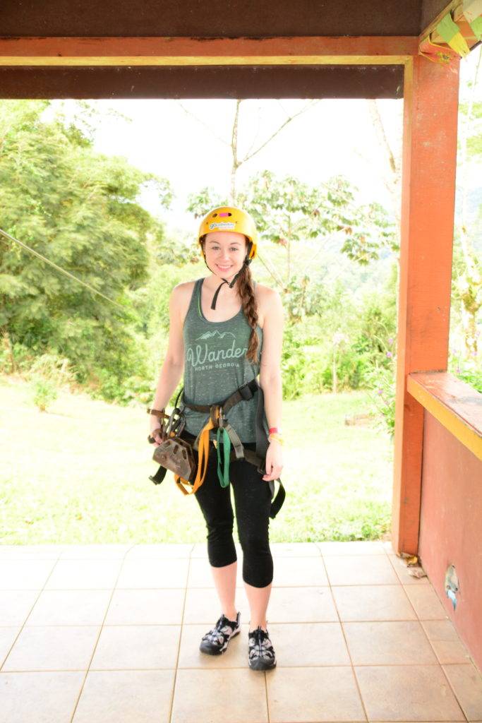 girl posing in zip line gear with harness and belay glove and helmet