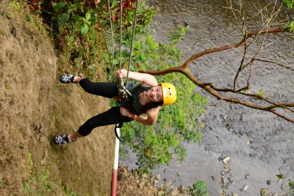 girl rappelling down a cliffside with a dark river below