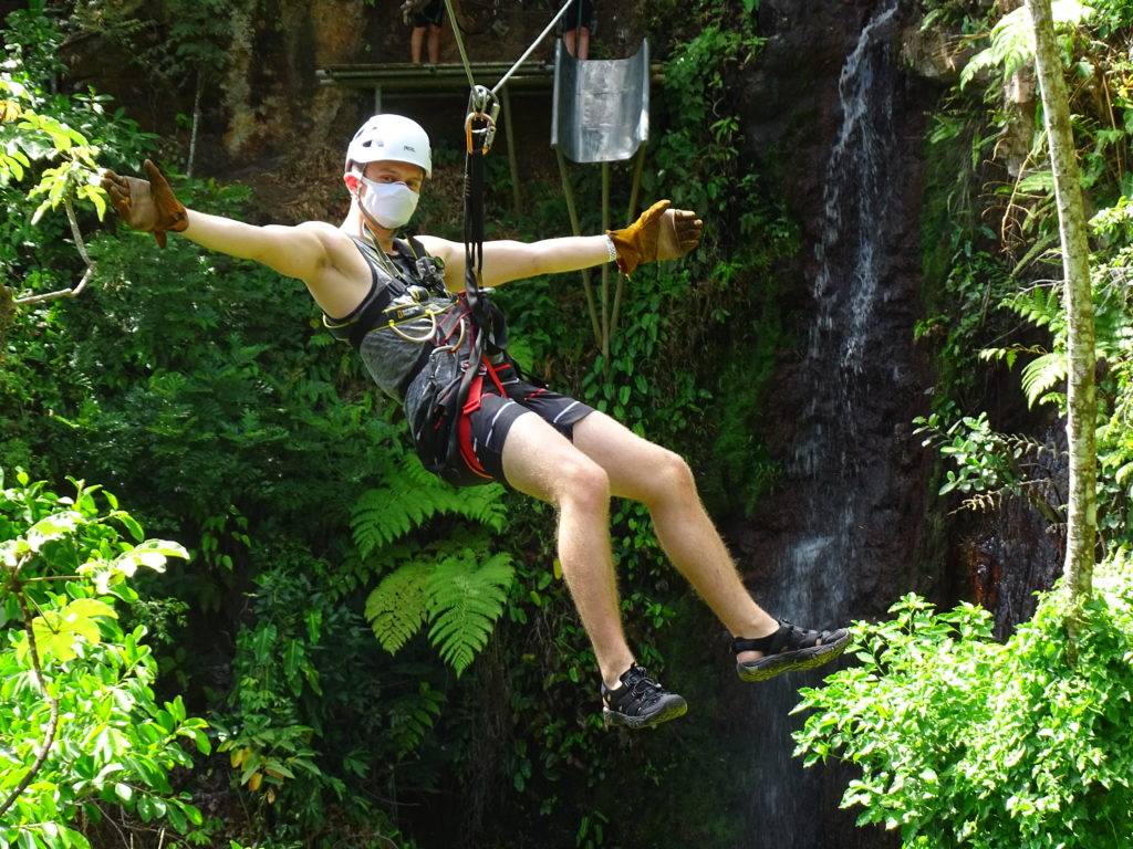 Man on a zipline with a waterfall and tropical foliage in the background at Rincon de la Vieja National park