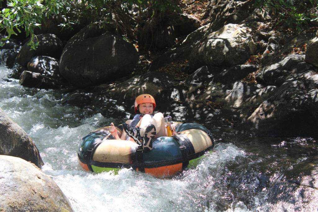 Smiling girl in a blue, white, green, and orange inner tube shooting down rapids