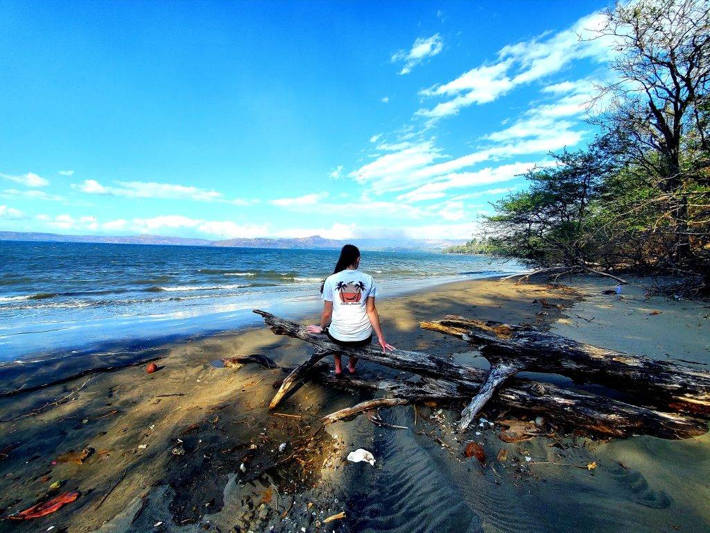 Girl sitting on driftwood on a black sand beach at high tide