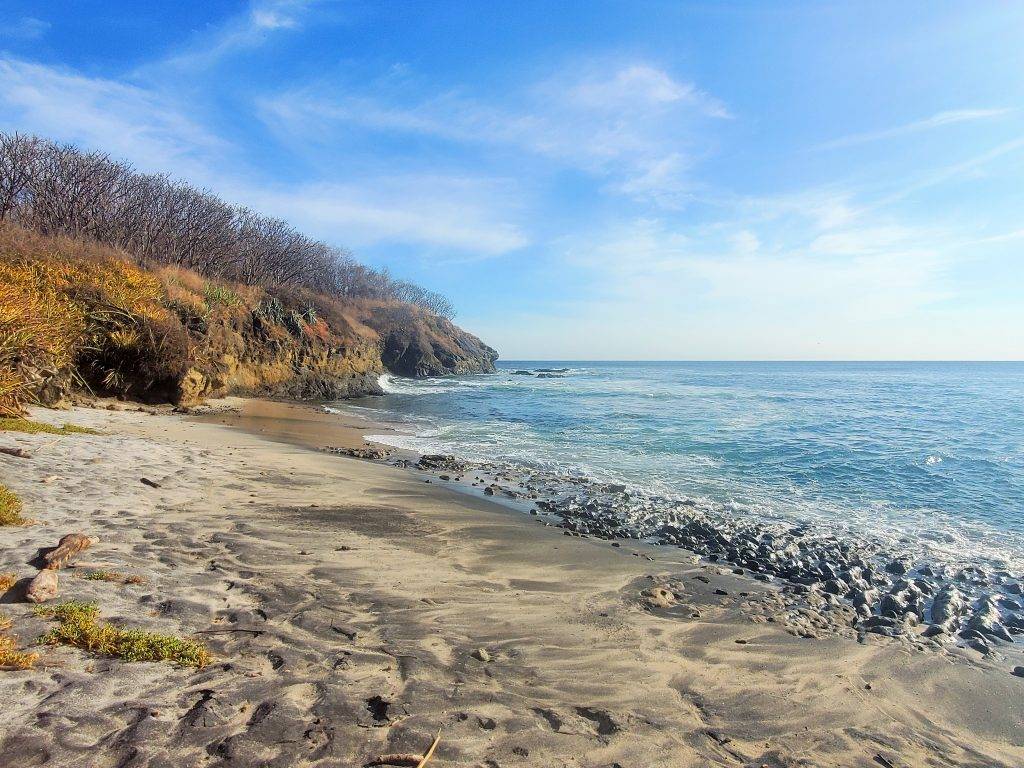 black and white sand beach with a lava rock shoreline and blue water