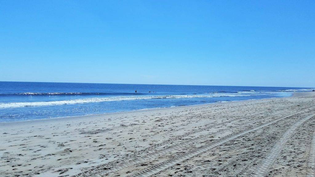 sandy beach with tire tracks and blue ocean in the background