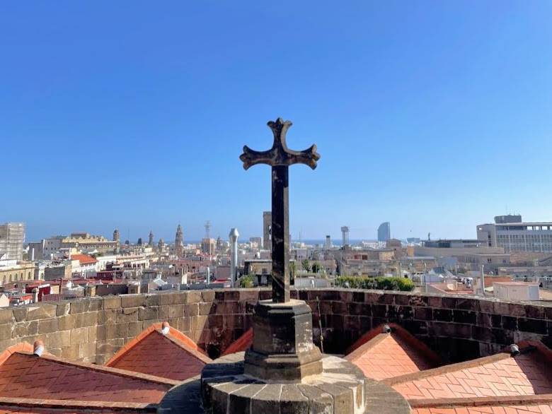 A cross on a rooftop with a view of Barcelona in the background