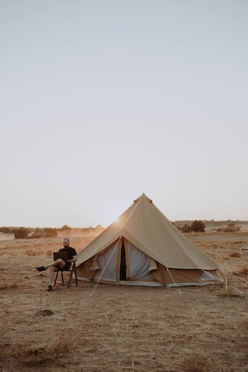 man working with laptop near tent; digital nomad