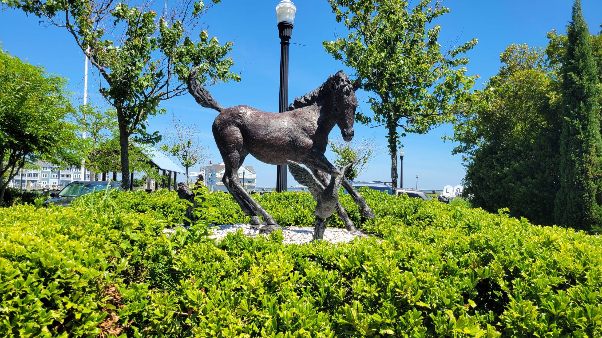statue of a wild pony against a green hedge and blue sky