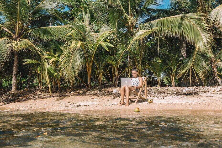 a woman working on the beach while sitting on a wooden chair