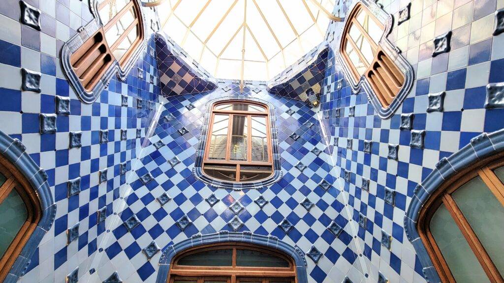 light shaft with dark and light blue checkered tiles and wood paneled windows and vents. Casa Batllo