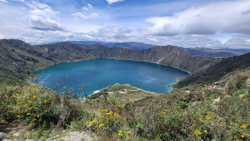 The Quilotoa Crater Lake under a cloudy sky with yellow wildflowers in the foreground