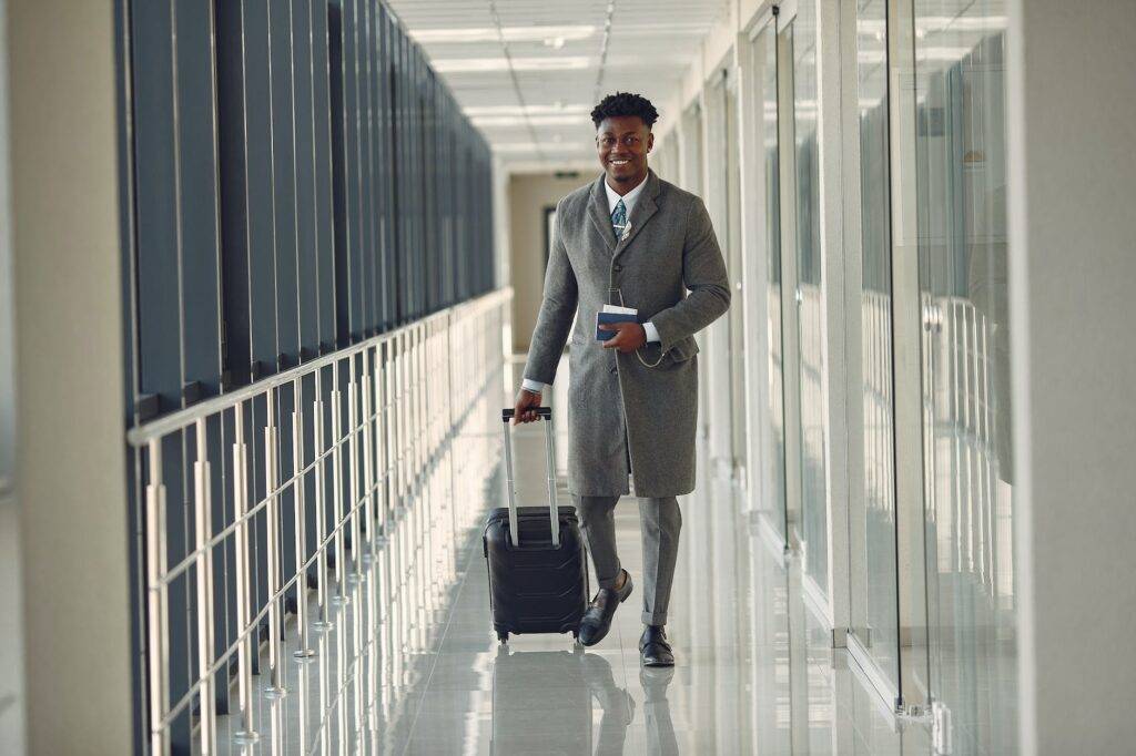 stylish man with suitcase and passport walking along airport corridor