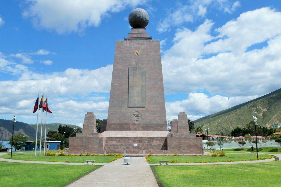 Middle of the world monument under a blue sky with green grass