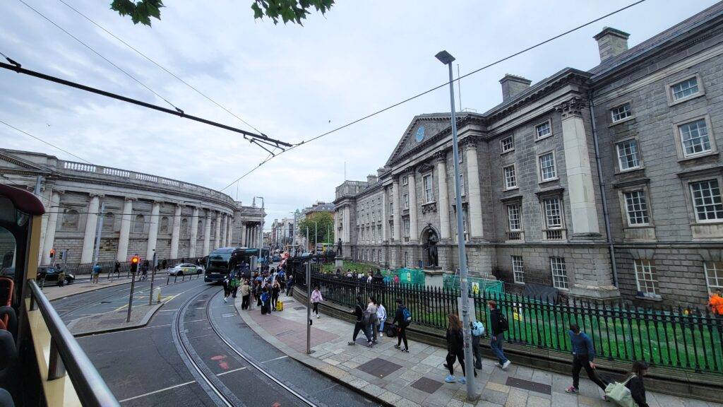 Exterior of Trinity College and the side of a red Big Bus Tours bus