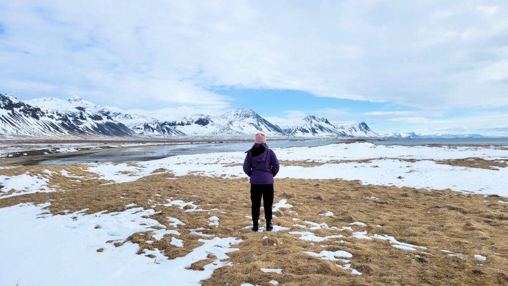 Girl standing in a snowy field with mountains and a fjord in the background. iceland