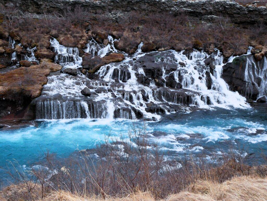 cascading waterfalls flowing from lava rock into a blue river