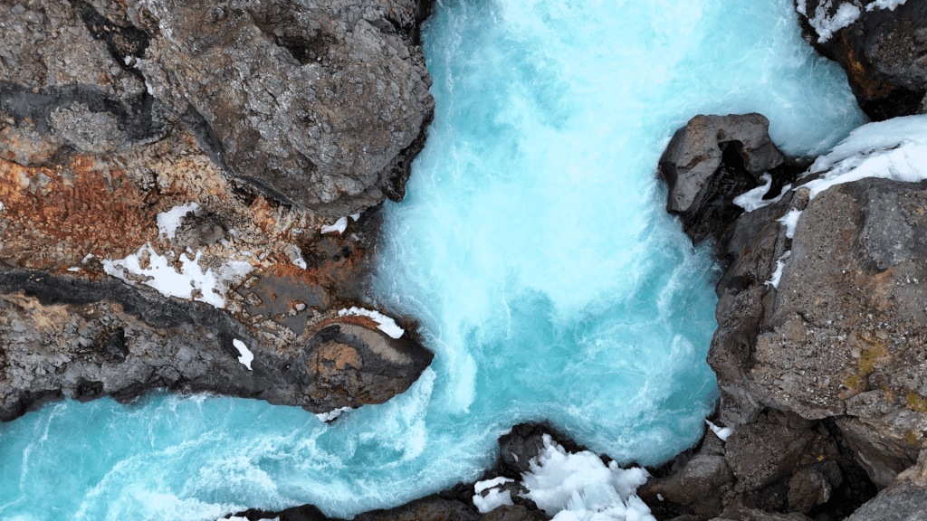 drone view of bright blue water surrounded by lava rock in Iceland