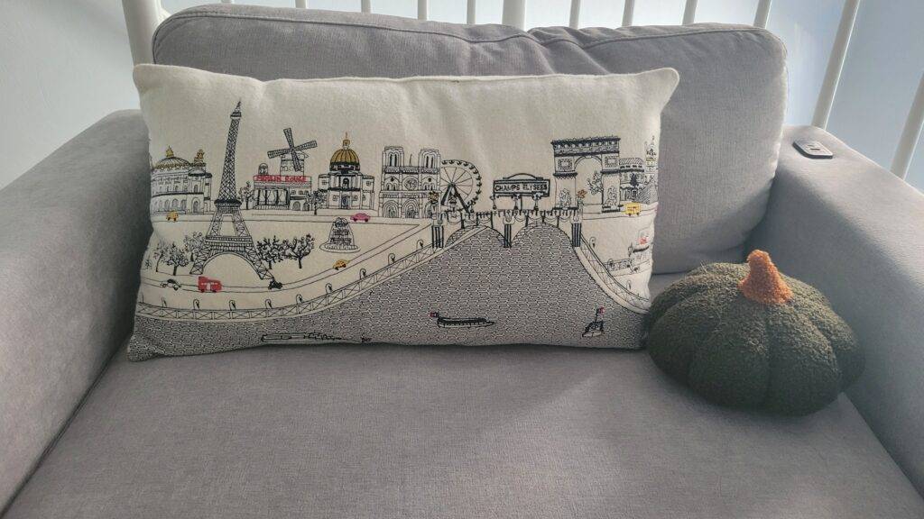 Embroidered pillow on a large chair with a green pumpkin pillow